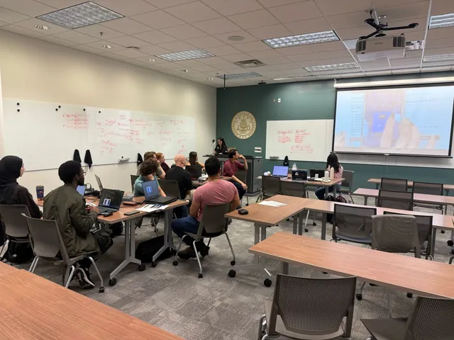 The whole room at laptops during the Bell state lab, facing a presenter at the podium and the Qubi worksheet on the projector.